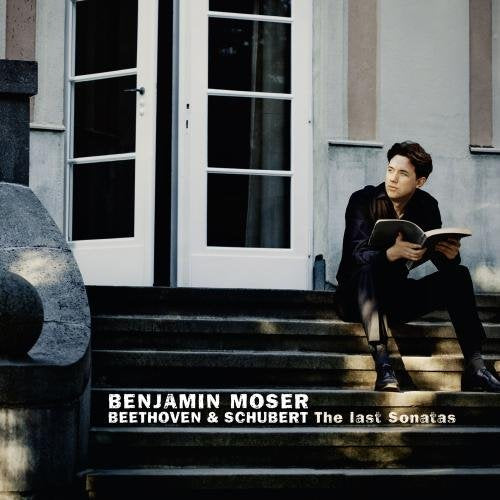 Man in black sits on steps, reading a book, beside a white door.