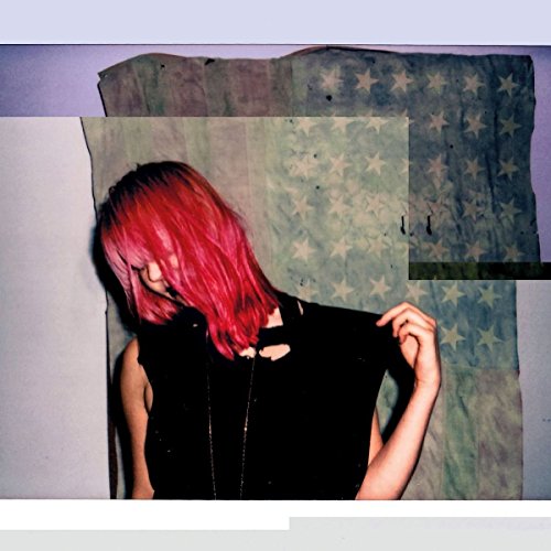 Red-haired person in black clothing partially obscuring a faded American flag.
