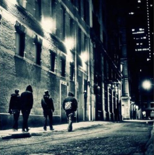 A black and white image of three people walking down a dimly lit city alleyway.