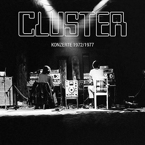 Black and white vinyl album cover with two musicians on stage surrounded by equipment.
