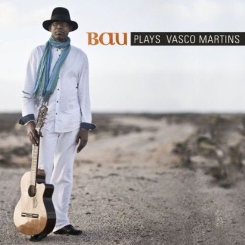 Man in white suit and hat holds guitar, standing on a desert road.