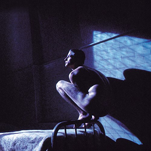 Man with large wings crouching in a dimly lit, tiled room.