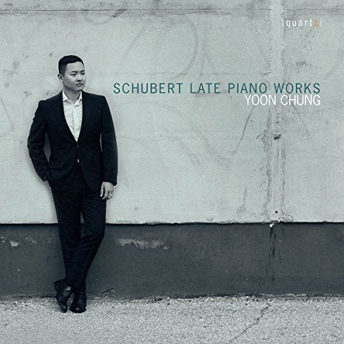 Man in a black suit leans against a gray concrete wall on a CD cover.