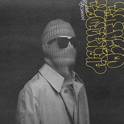 Person in knit mask and sunglasses, with yellow graffiti text.
