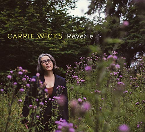 Woman in a field of purple flowers, wearing glasses and a dark jacket.