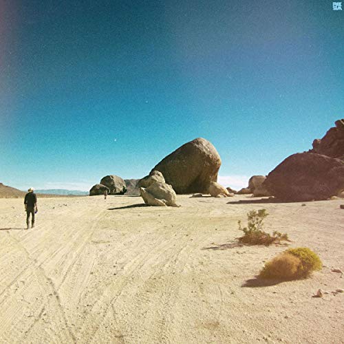 Desert landscape with large rocks and a lone figure walking away.