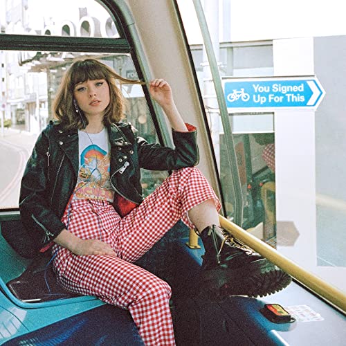 Maisie Peters poses on a bus, wearing a leather jacket and red gingham.