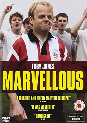 Toby Jones in a red and white rugby shirt with people in the background.