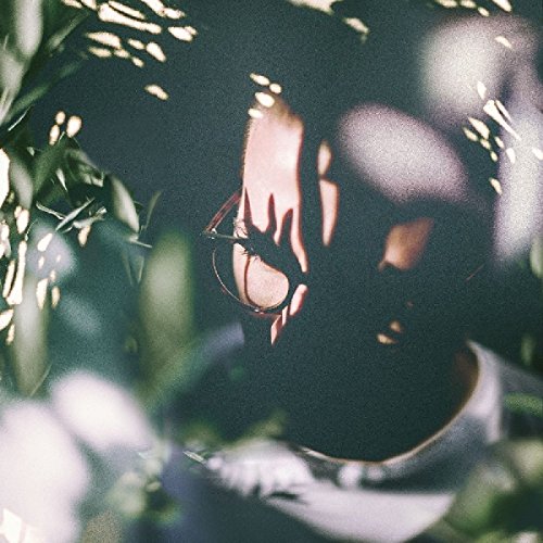 "CD album cover with a person wearing glasses surrounded by foliage and dappled light."