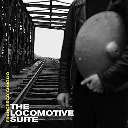 Person holding a train wheel, railroad tracks under a metal bridge.