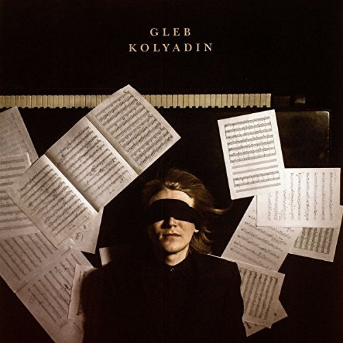 "Album cover featuring a man blindfolded, surrounded by scattered sheet music on a black background."