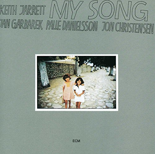 "Album cover with two girls on a stone path, grey background, artist names at top."