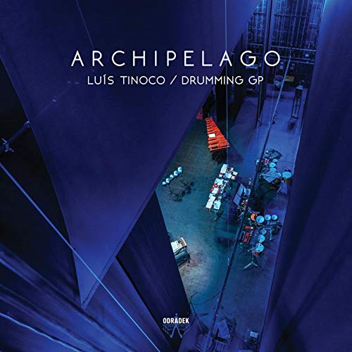 The image is a CD cover for "Archipelago" by Luís Tinoco. #### Alt Text "CD cover with aerial view of drum kits between tall, blue-lit buildings."