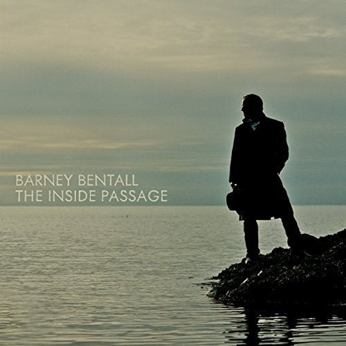 Album cover: silhouette of a man standing on a rocky shore, holding a hat.