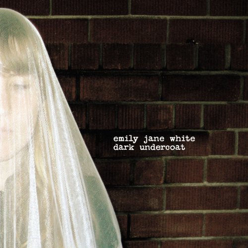 A woman's face is partially obscured by a white veil against a brick wall.