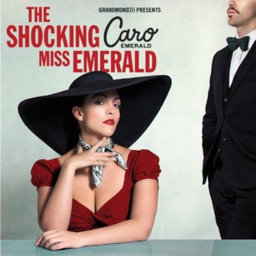 A woman in red dress and large hat sits beside a man in a tuxedo.