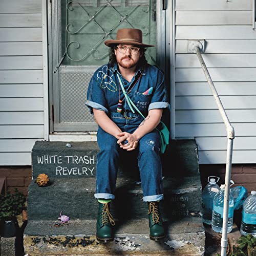 Man in denim overalls and hat sitting on concrete steps.