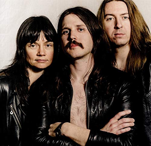 Three musicians with long hair pose in leather jackets against a white background.