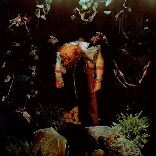 Person with curly hair surrounded by fish and foliage in darkness.