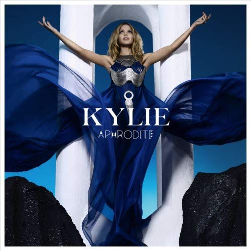 Kylie Minogue in blue dress, arms outstretched, with Grecian columns.