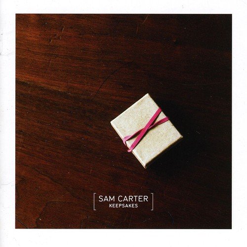 A square album cover featuring a small gift box on a wooden surface.