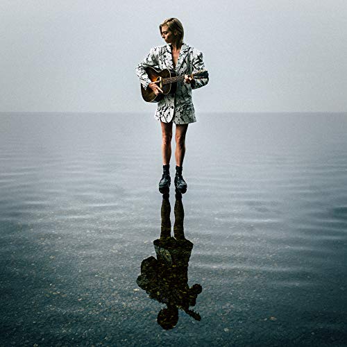 A woman stands on calm water, playing guitar, with a reflective surface below.