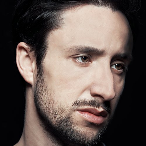 Close-up portrait of a man with dark hair and a beard.