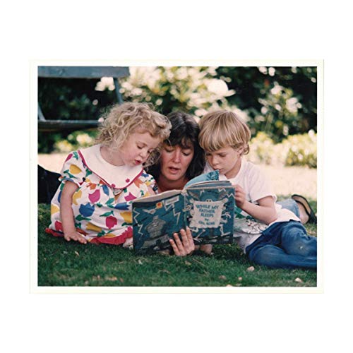 Woman and two children reading a book on the grass.