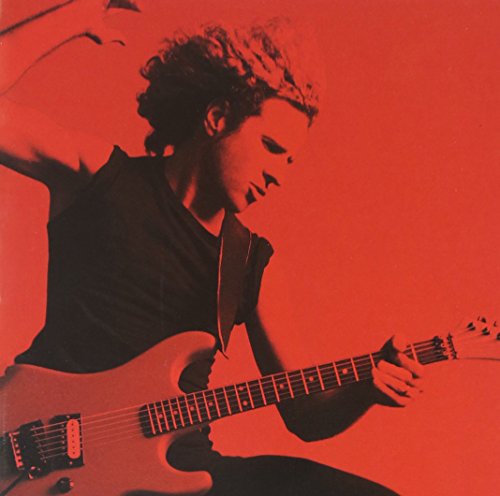 Sammy Hagar playing a light-colored electric guitar against a red background.