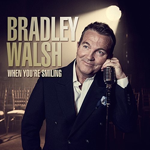 Man in a suit holding a vintage microphone, smiling, on a CD cover.