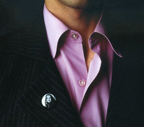 A man in a black suit jacket and pink shirt with a pin on the lapel.