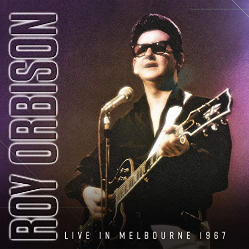 Roy Orbison in sunglasses performing with a guitar and microphone.
