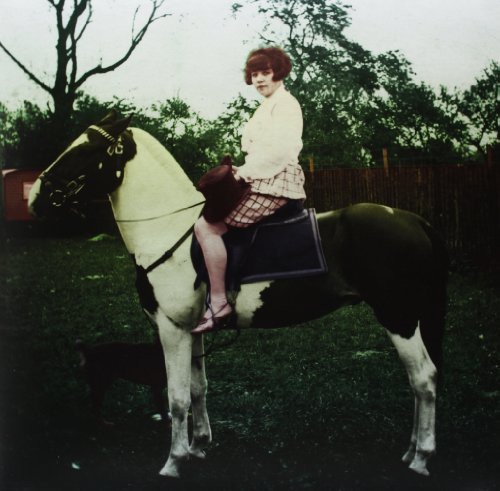 Woman with red hair riding a paint horse in a field.