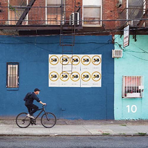 A vinyl record cover featuring a man riding a bike past a blue and teal building.