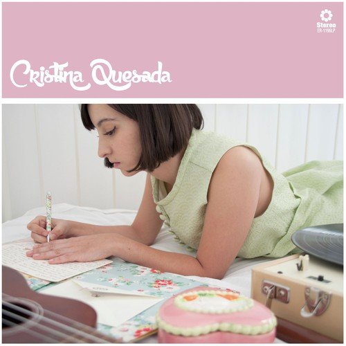 A woman lies on a bed, writing, with a record player and cake nearby.