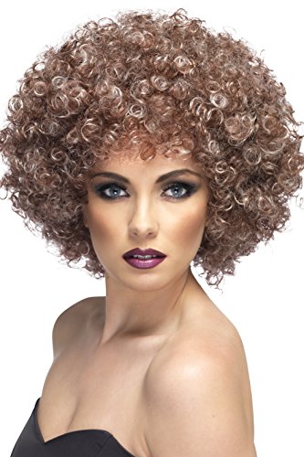 A woman wearing a curly, reddish-brown afro wig and dark makeup against a white background.