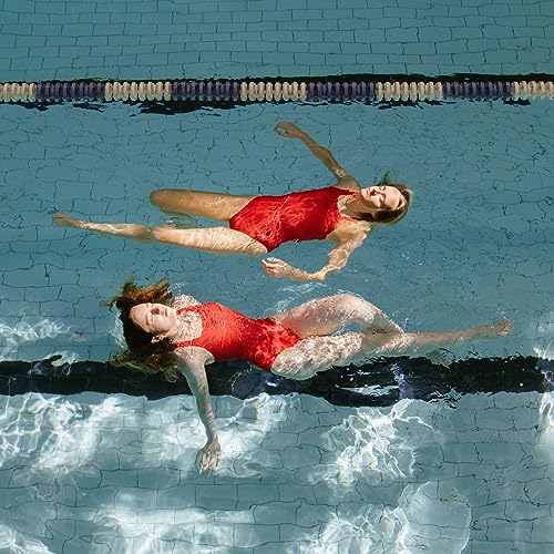 Two women in red swimsuits float underwater in a blue pool.