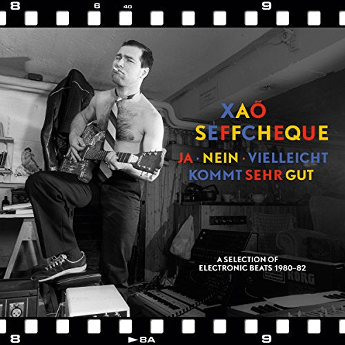 "Album cover with a man playing guitar, surrounded by music equipment, in a room."