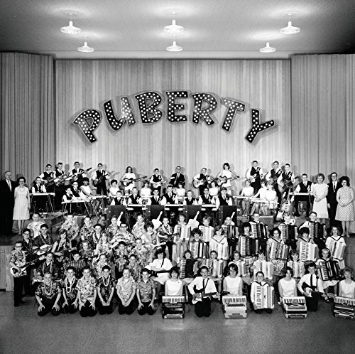 "Black and white image of a large group posing under 'PUBERTY' sign."