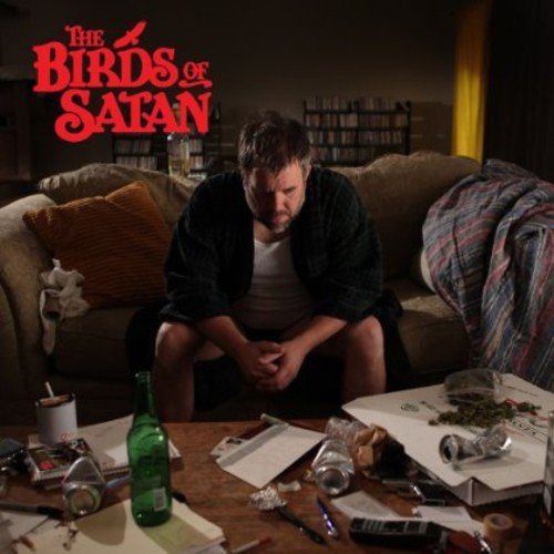 "Man sitting on couch, surrounded by clutter, with 'The Birds of Satan' title."