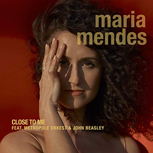 The alt text for the image is: "Album cover featuring a woman with curly hair against a red background."