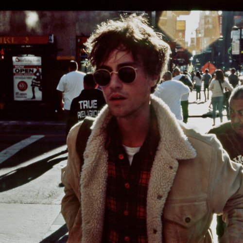 Man wearing sunglasses and a sheepskin jacket, standing on a busy city street.