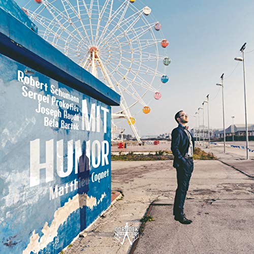 A man in a suit stands beside a blue wall with white text, near a Ferris wheel.