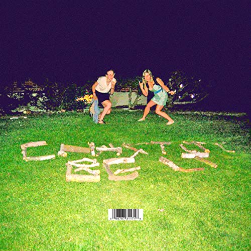 Two women on grass next to letters spelling "CHASTITY" at night.