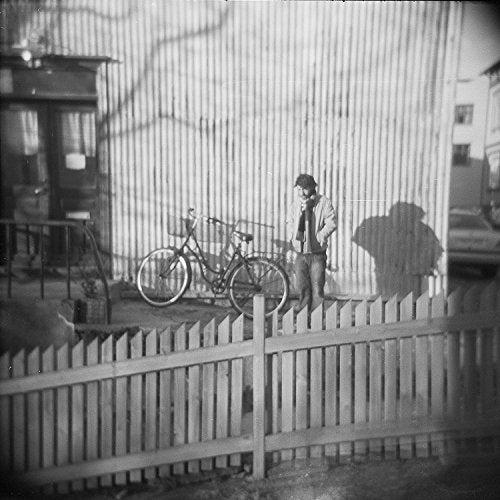 Black and white photo of a man with a bicycle near a fence.