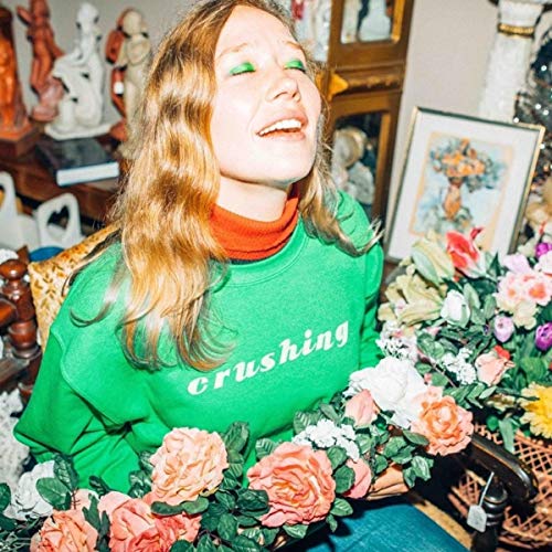 A woman in a green "crushing" sweatshirt sits surrounded by flowers and decorative items.