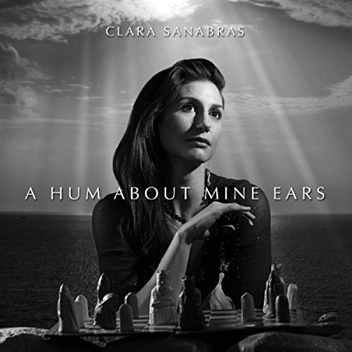 Black-and-white album cover with woman surrounded by chess pieces on a beach.