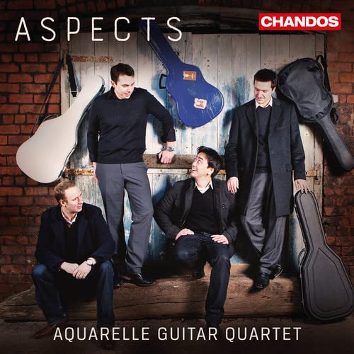 Four musicians with guitars pose in front of a weathered brick wall.