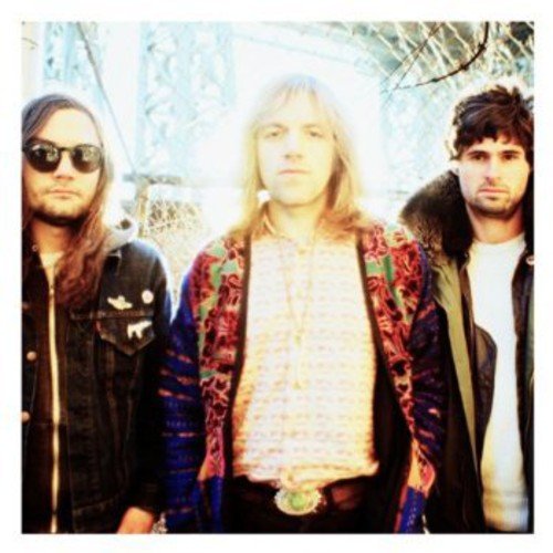 The image shows three men standing side by side, looking directly at the camera.