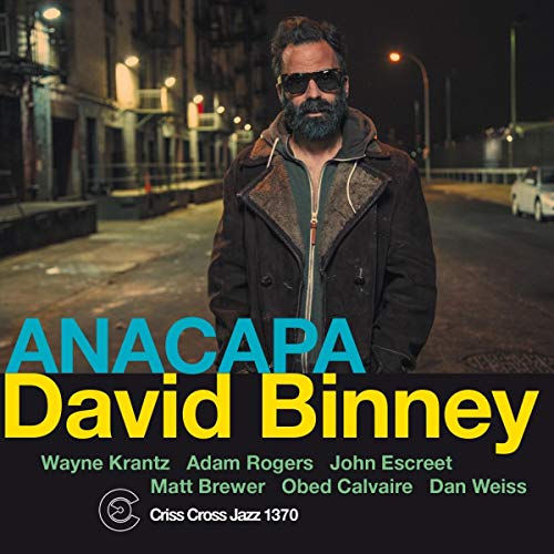 "Album cover with a man in a dark jacket standing on a city street at night."